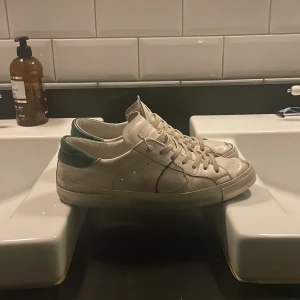 Vita sneakers från Philippe Model - Snygga vita sneakers från Philippe Model med gröna detaljer. Skorna har snörning och en klassisk design som passar perfekt till vardags. Sulan är grön undertill vilket ger en cool kontrast. Perfekta för en avslappnad stil.