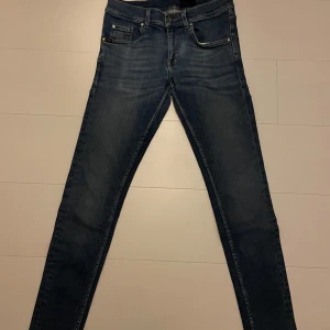 Blå jeans från Tiger of Sweden - Snygga blå jeans från Tiger of Sweden med klassisk femficksdesign och knappgylf. Perfekta för en stilren look. Märkeslapp i läder baktill.
