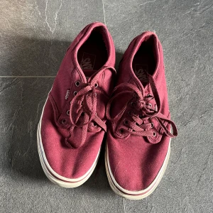 Vinröda sneakers från Vans - Säljer ett par vinröda Vans sneakers med klassisk design och snörning. Skorna har en vit sula och är perfekta för en avslappnad stil. Smått smutsiga sulor men sparsamt använda.