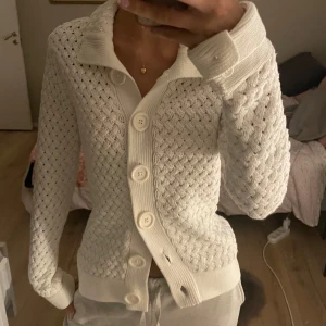 Vit stickad kofta med stora knappar - Säljer en stilren vit stickad kofta med stora knappar framtill. Koftan har ett fint mönster och långa ärmar, perfekt för kyligare dagar. Den har en klassisk krage och ribbade muddar vid ärmslut och nederkant. Den är M men den passar som en S!