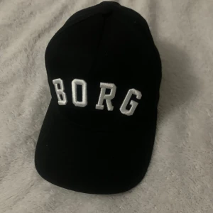 Svart keps - Snygg svart keps med vit broderad text 'BORG' framtill. Perfekt för en casual look och skydd mot solen. Justerbar passform för optimal komfort.