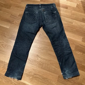 Mörkblå jeans med slitningar - Snygga mörkblå jeans med slitningar och fransar vid bensluten. De har en klassisk femficksdesign och tydliga sömmar på bakfickorna. Perfekta för en avslappnad stil.