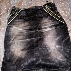 Kort kjol  - Snygg svart kjol med subtilt mönster och kontrastsömmar i gult. Kjolen har en slits baktill och dekorativa fickor framtill. Perfekt för en trendig look.