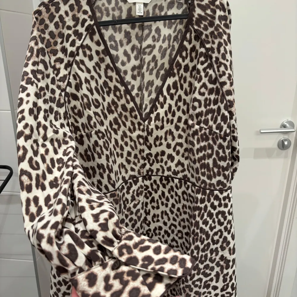 Snygg leopardmönstrad klänning med v-ringning och långa ärmar. Perfekt för att sticka ut med ett djärvt mönster. Klänningen har en bekväm passform och är lätt att styla för olika tillfällen.köpt för en månad sen och använd en gång dessvärre för stor . Mekot.