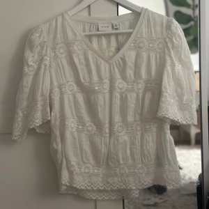 Vit blus från Vila - Somrig vit blus från Vila med v-ringning och korta ärmar. Blusen har fina spetsdetaljer. Perfekt för en somrig look!