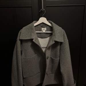 Haft i typ 1 år använt extremt lite bara nån gång. Snygg grå kappa från Kappahl i storlek L. Den har en klassisk krage och knappar framtill. Perfekt för en stilren look. Två stora fickor framtill.