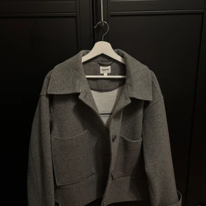 Grå kappa från Kappahl - Haft i typ 1 år använt extremt lite bara nån gång. Snygg grå kappa från Kappahl i storlek L. Den har en klassisk krage och knappar framtill. Perfekt för en stilren look. Två stora fickor framtill.