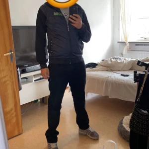 Svart bomberjacka från Hugo Boss - Säljer en snygg svart bomberjacka från Hugo Boss. Jackan har en dragkedja framtill och är dekorerad med gröna detaljer. Perfekt för höst och vår, med en normal passform. Den är i mycket bra skick och redo för nya äventyr!