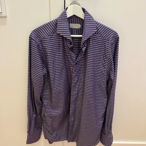 Rutig skjorta från Eton - Säljer en stilren rutig skjorta från Eton i storlek M. Skjortan har en snygg kombination av blå och rosa rutor och är i slim fit. Perfekt för både vardag och fest! Den är långärmad och har klassiska knappar framtill. Passar utmärkt till både jeans och kostymbyxor.