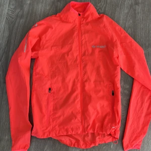 Neonorange vindjacka från soc - Säljer en supercool neonorange vindjacka från soc. Perfekt för löprundan eller cykelturen! Jackan har en dragkedja framtill och två praktiska fickor med dragkedjor. Den är lätt och smidig, perfekt för vår och höst. Passformen är normal och den har långa ärmar. Ett måste för den aktiva! 🧡