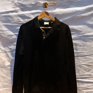 Svart tröja från Burberry - Säljer en stilren svart tröja från Burberry. Den har en klassisk krage och är perfekt för både vardag och fest. Tröjan är i mycket bra skick och har en diskret Burberry-ruta på insidan av kragen. Passar perfekt för höst och vinter!