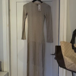 Glittrig ribbad långklänning - Säljer en superfin beige ribbad långklänning i nytt skick med lapp kvar. Klänningen är långärmad och gjord av ett glittrigt material