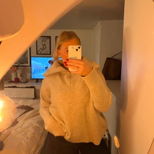 Beige stickad tröja med hög krage - Mysig beige stickad tröja med en hög krage som är perfekt för kyliga dagar. Tröjan har långa ärmar och en avslappnad passform som gör den superbekväm. Perfekt för både höst och vinter!