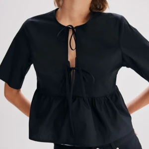 Svart blus med knytband - Snygg svart blus med knytband framtill. Den har korta ärmar och en lös passform som ger en avslappnad look. Perfekt för både vardag och fest! 