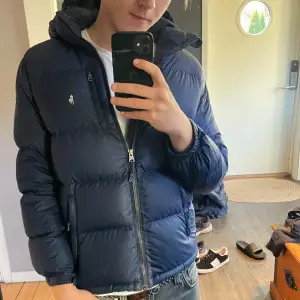 Säljer en snygg mörkblå dunjacka i mycket bra skick från Ralph lauren. Jackan har en dragkedja framtill och en liten logga på bröstet. Perfekt för kyliga dagar och passar både till vardags och lite finare tillfällen. Den är varm och bekväm med en normal passform. Storleken är M ungdom passar xxs