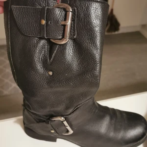 Svarta skinnstövlar med spännen 38-38,5 - Snygga svarta stövlar i skinn med coola spännen och dragkedja på sidan. Perfekta för höst och vinter, de ger en tuff look till vilken outfit som helst. Skorna är i bra skick och redo för nya äventyr!