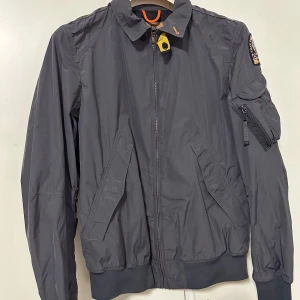 Grå bomberjacka från Parajumpers - Säljer en snygg grå bomberjacka från Parajumpers i mycket bra skick. Kvittot finns tyvärr inte men lapparna finns kvar + Scan i jackan finns för att vissa att den är äkta!!  Köpt för flera år tbx har bara legat hemma i onödan därav den säljs   Det är barnstorlek L - menas med XS/S  Jackan är i fint skick 