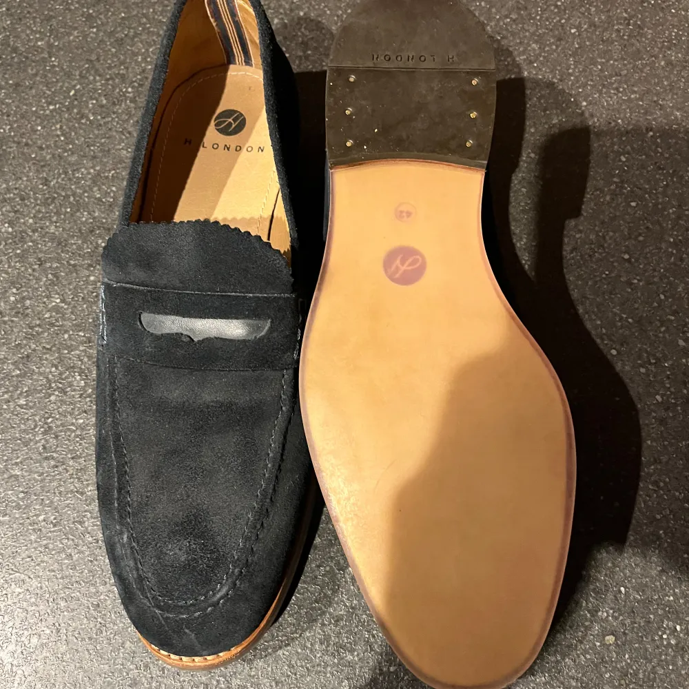 Snygga marinblå loafers i mocka från Hudson London. De har en klassisk design med en stilren söm och en bekväm innersula. Perfekta för både vardag och festliga tillfällen. Sulan är i ljust material som ger en fin kontrast till det mörka mockaskinnet.. Skor.