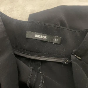 Svarta byxor från Bik Bok - Säljer ett par svarta kostymbyxor från Bik Bok i storlek 34. De har en klassisk design med en rak passform och hög midja, perfekt för både vardag och fest. Materialet känns mjukt och bekvämt. Passar utmärkt till höst- och vintergarderoben.