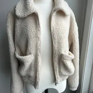 Säljer en supermysig beige teddyjacka från Pull&Bear. Den har en dragkedja framtill och två praktiska fickor. Perfekt för höst och vinter när du vill hålla dig varm och stilren. Jackan är långärmad och har en skön krage. Passar perfekt för en casual look!