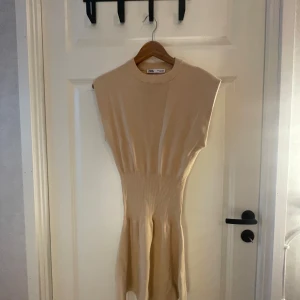Beige klänning från Zara - Säljer en superfin beige klänning från Zara. Den är ärmlös och har en tight passform upptill med en ribbad midja som ger en snygg siluett. Perfekt för både vardag och fest! 💫