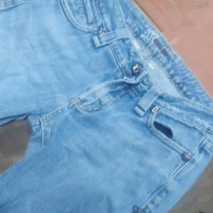 Blå jeans med pärldetaljer - Säljer ett par snygga blå jeans med unika pärldetaljer på bakfickorna. De har en klassisk femficksdesign och är gjorda i bomull med lite stretch för extra komfort. Perfekta för en cool och avslappnad stil!