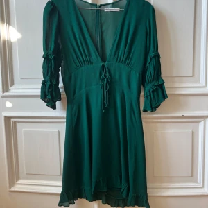 Reformation klänning smaragd grön - En vacker grön klänning med puffärmar och en djup V-ringning. Klänningen har en snörning i midjan och en volang vid nederkanten. Storlek S Aldrig använd