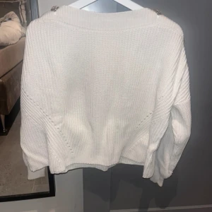 Guess tröja  - Vit, stickad tröja från Guess med guldknappar vid axlarna. Använd ett fåtal gånger, storlek 40 men känns mer som en 38.
