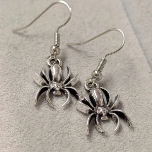 Silvriga spindelörhängen - Coola och unika örhängen i form av spindlar, perfekta för att ge din outfit en edgy touch. De är gjorda i silverfärgat material och har en detaljrik design.ny