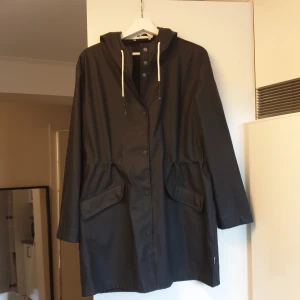 Svart regnjacka med huva - Marinblå regnjacka med huva och vita snören från Only. Jackan har långa ärmar och knappar framtill. Dragsko i midjan och praktiska fickor. Längre modell. Sparsamt använd. Nypris 500kr