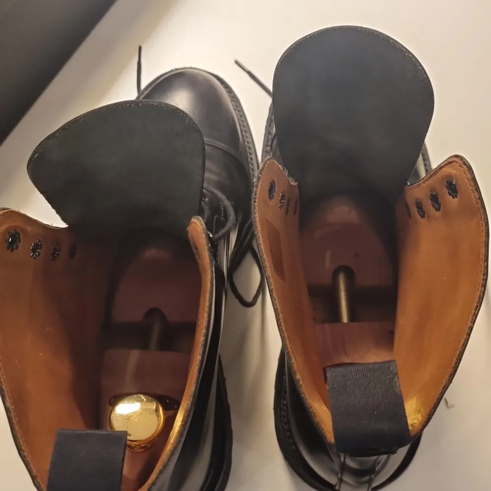 Säljer ett par stilrena svarta boots från Crockett & Jones. De är i skinn och har en klassisk snörning framtill. Skorna har en robust sula från Vibram, perfekt för höst och vinter. Insidan är fodrad i en ljusare nyans för extra komfort. Perfekta för både vardag och mer formella tillfällen.. Skor.