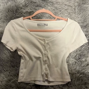 Vit ribbad kortärmad topp - Säljer en superfin vit ribbad topp från Lager 157 i storlek XS. Den har korta ärmar och knappar framtill, vilket ger en söt och stilren look. Perfekt för både vardag och fest!