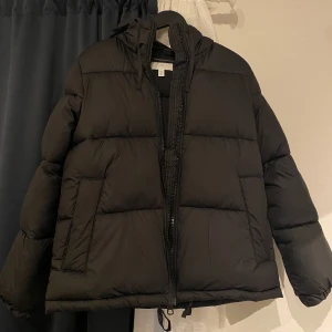 Svart pufferjacka med Huva - H&M  - En jättefin svart pufferjacka med huva som är i mycket bra skick. Använd 5-7 gånger och har inga defekter. Har både inre och yttre fickor som är ganska stora. Väldigt tjock och varm jacka som passar perfekt till vintern. Skriv gärna vid frågor! 🫶
