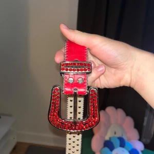 Rött glittrigt bälte - Säljer ett supercoolt rött bälte med massor av glittriga detaljer. Bältet har en stor, blingig spänne som verkligen drar blickarna till sig. Perfekt för att liva upp vilken outfit som helst! Passar både till fest och vardag.