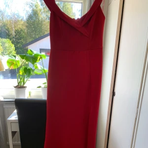 Röd långklänning från Goddiva - Säljer en elegant röd långklänning från Goddiva. Klänningen har en vacker draperad detalj vid halsen och en smickrande passform. Perfekt för festliga tillfällen! Den är i nyskick och har en dragkedja i ryggen för enkel påklädning.