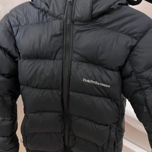 Svart dunjacka från Peak Performance (nypris ca 2000-3000kr) - Vinterjacka från peak performance köpt för ca 2 år sen. Säljer pga lite för liten, jackan är i storlek 150(skriv om du vill ha mått). Den är i fint skick men har fått ett märke av färg på baksidan nedtill. Sen har även en av fickornas ände på dragkjedjan lossnat(se bild). Detta går nog att reparera för den som vill. Jackan har även en innerficka och en justering på insidan. Nypris 2000-3000, säljer för 550kr, värmer väldigt bra.