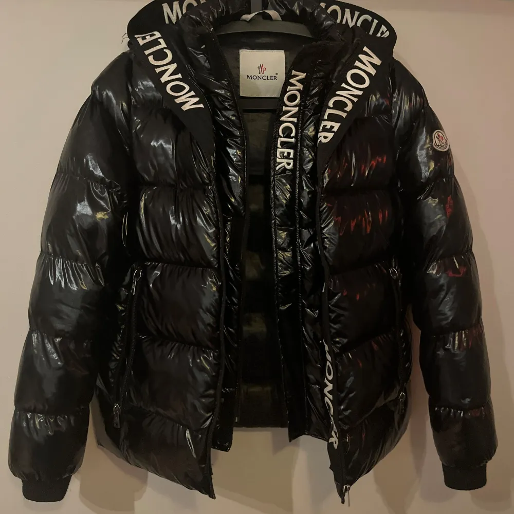 Säljer en snygg svart dunjacka från Moncler i bra skick. Jackan har en glansig finish och Moncler-logga på vänster ärm. Den är långärmad med dragkedja och har coola Moncler-band längs med dragkedjan. Perfekt för vintern! Den har två dragkedjor varav ena låter märket MONCLER synas längst med. Den yttre dragkedjan har en liten skada längst ner, påverkar inte funktionen märkbart. Serien på insidan har lossnat något. . Jackor.