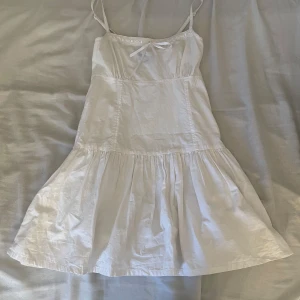 Vit klänning från Motel - Söt vit klänning från Motel i storlek XS. Den har smala axelband och en liten rosett framtill. Perfekt för sommardagar eller en avslappnad fest. Klänningen är i ett lätt och bekvämt material som ger en luftig känsla.