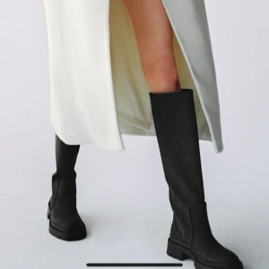 Svarta höga boots - Snygga svarta höga boots i syntetmaterial med en chunky sula. Perfekta för höst och vinter, dessa boots ger en cool look och är superbekväma att gå i. De har en stilren design utan snörning eller dragkedja, vilket gör dem lätta att ta på och av.