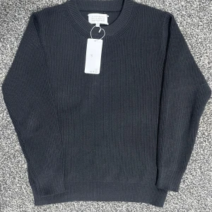 Svart stickad tröja från Maison Margiela - Säljer en stilren svart stickad tröja från Maison Margiela i storlek S. Tröjan är i nytt skick med etikett kvar. Perfekt för höst och vinter med sin varma och bekväma passform. Tillverkad i Italien med högkvalitativt material. Passar både till vardags och mer uppklädda tillfällen.