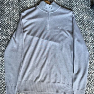 Stickad grå J Lindeberg zip tröja - En grå J Lindeberg halzip tröja i storlek M. Tröjan har en liten J Lindeberg logga vid bröstet. Den är helt ny, lappen finns kvar.  Nypris: 1500kr  Mitt pris: 999kr