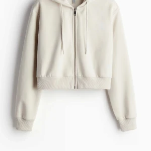 Beige croppad hoodie - Säljer en supermjuk och stilren beige croppad hoodie med dragkedja och huva. Perfekt för en avslappnad look! Den har långa ärmar och ribbade muddar för extra komfort. Passar perfekt till både jeans och leggings. 🧥✨