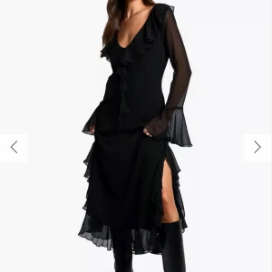 Svart långklänning med volangdetaljer - Snygg svart långklänning med volangdetaljer och v-ringning. Klänningen har långa ärmar i ett mesh-tyg och en slits på sidan för extra stil. Perfekt för festliga tillfällen!