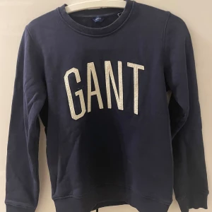 Mörkblå sweatshirt från GANT - Säljer en snygg mörkblå sweatshirt från GANT i storlek XS. Tröjan har ett stort GANT-tryck i vitt på framsidan och är i mycket bra skick. Perfekt för höst och vinter, med långa ärmar och mjukt material. Har inget slitage❄️💙
