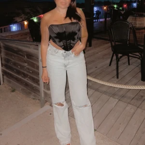 Svart korsett i sammet - Snygg svart korsett i sammet som är perfekt för en utekväll. Den är axelbandslös och har en tight passform som framhäver figuren. Passar bra till både jeans och kjol för en stilren look.