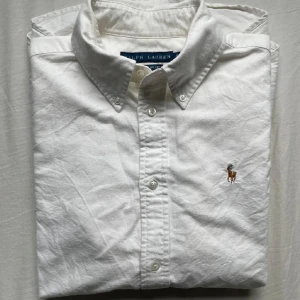 Vit skjorta från Ralph Lauren - Säljer en klassisk vit skjorta från Ralph Lauren i bomull. Skjortan har långa ärmar och en broderad logga på bröstet. Perfekt för både vardag och fest 🎉Den har en snygg och stilren design med knappar framtill. Inga fläckar eller svettfläckar. Nypris ≈ 1800 storlek: xs hör av dig vid frågor💯