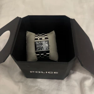 Klocka - Säljer en stilren klocka från Police i silver. Den har en fyrkantig urtavla med ett unikt mönster och en robust länkarmband. Perfekt för både vardag och fest! Kommer i originalförpackning.