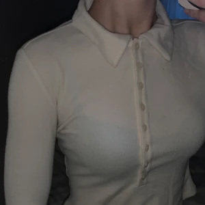 Vit/Beige ribbad polotröja - Säljer en ribbad polotröja med knappar framtill. Tröjan är långärmad och har en tight passform. Den är i mycket bra skick och passar både till vardags och lite finare tillfällen.