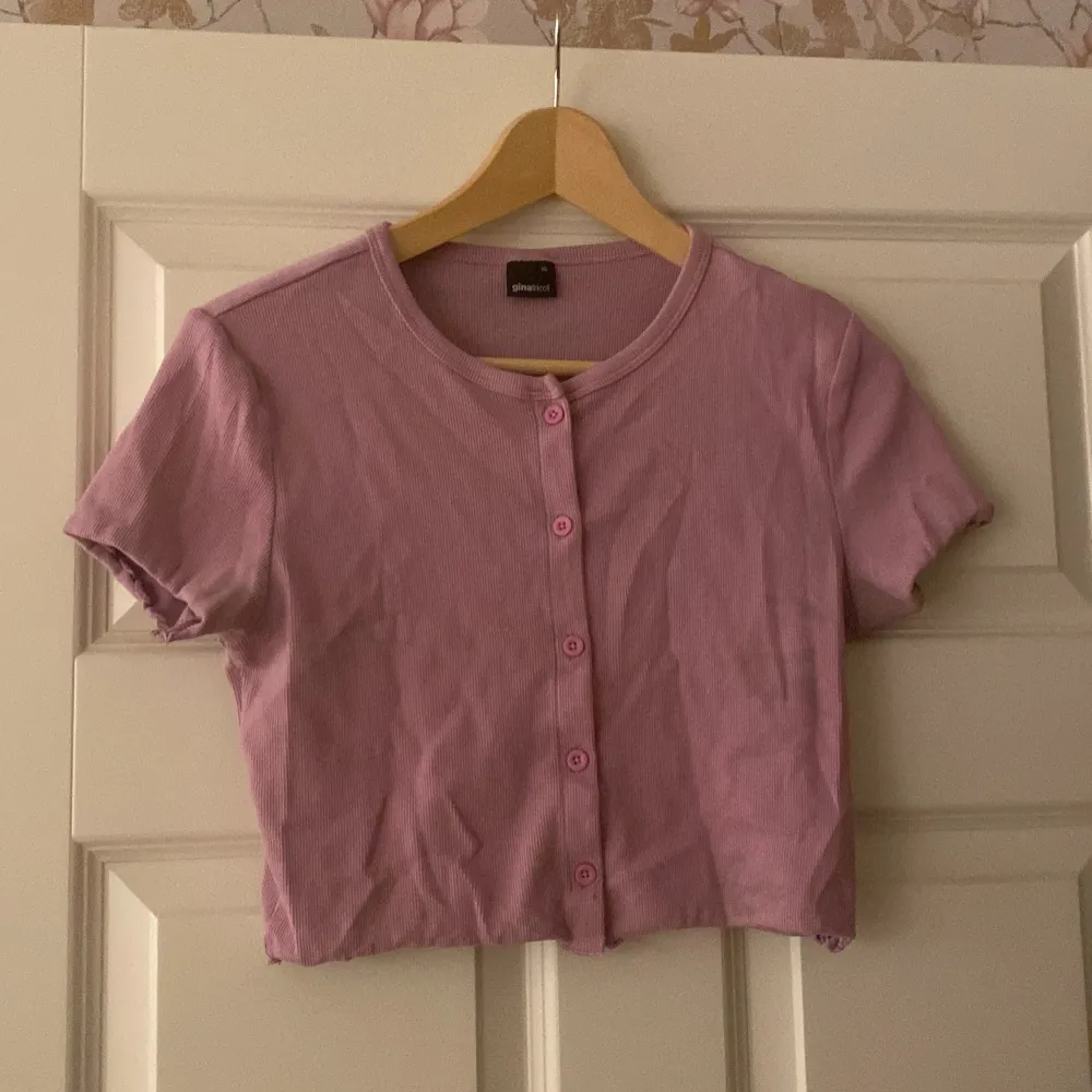 Säljer en söt rosa ribbad topp från Gina Tricot i storlek XL. Toppen har korta ärmar och knappar framtill, perfekt för en avslappnad sommarlook. Den är i bra skick och passar både till vardags och festliga tillfällen.. Toppar.