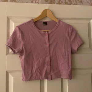 Rosa ribbad topp från Gina Tricot - Säljer en söt rosa ribbad topp från Gina Tricot i storlek XL. Toppen har korta ärmar och knappar framtill, perfekt för en avslappnad sommarlook. Den är i bra skick och passar både till vardags och festliga tillfällen.